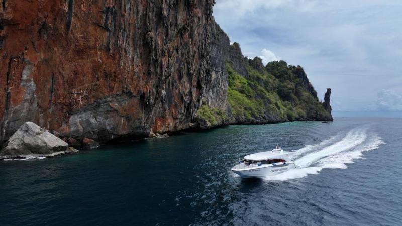 Speedboat traveling near large rocky cliff over blue water.