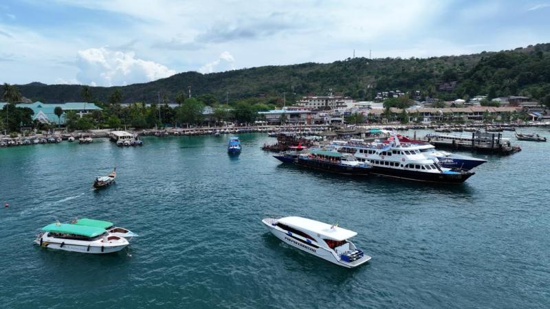 Boats anchored near a coastal town with lush hills in the background.