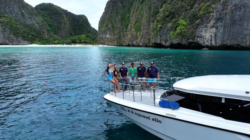 Group of people on a boat near towering cliffs and clear water.