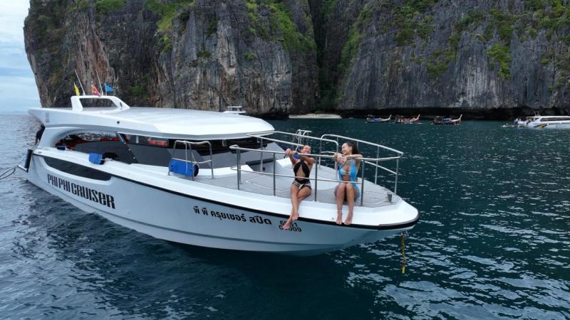 Two people relax on a boat near rocky cliffs in clear blue water.